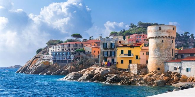 Vista del borgo marinaro di Giglio Porto, con case multicolori, un'antica torre difensiva e una costa rocciosa, Isola del Giglio, Toscana, Italia